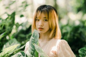 A girl with short hair and a pink shirt is standing in the woods