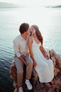 a man and a woman are sitting on a rock by the water