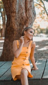 woman in yellow sleeveless dress standing near brown tree during daytime